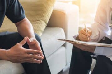 Doctor consulting male patient, working on diagnostic examination on men's health disease or mental illness, while writing on prescription record information document in clinic or hospital office